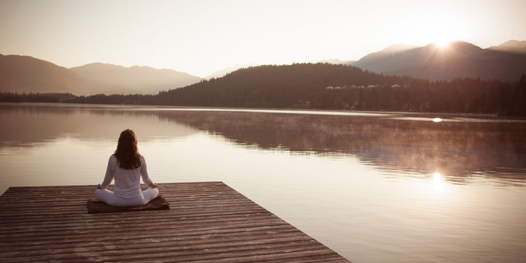 Frau auf einem Steg vor einem See beim Sonnenuntergang
